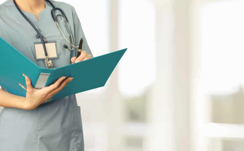 Medio cuerpo de una enfermera de pie firmando unos papeles en un hospital