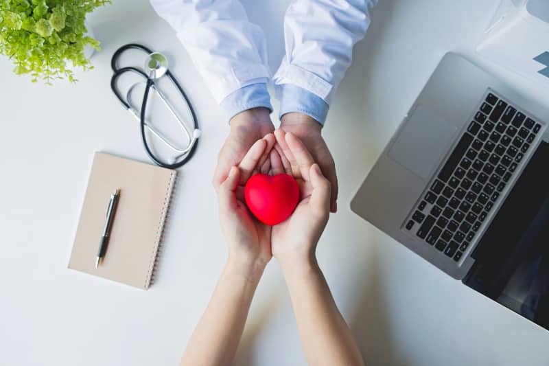 Vista superior médico y paciente manos sosteniendo corazón rojo sobre mesa blanca